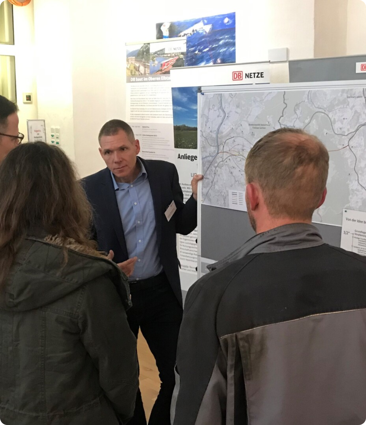 Michael Menschner, subproject manager of the Dresden to Heidenau section, stands at the whiteboard showing a map of the project area. He is facing three people who are looking at him and the map.