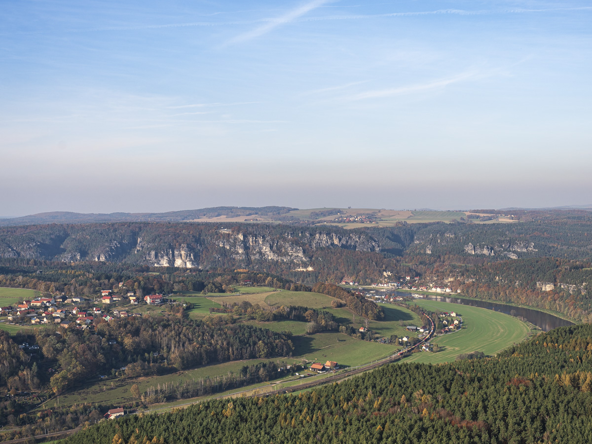 A wide view of the Elbe valley with trees, houses and typical sand stone hills in the background. 