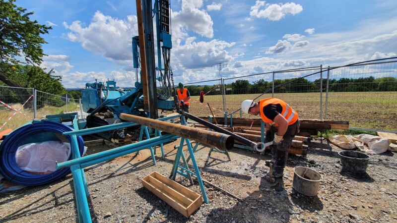 On a sunny day, two workers in high-visibility-vests are in the process of core drilling at a drilling construction site.