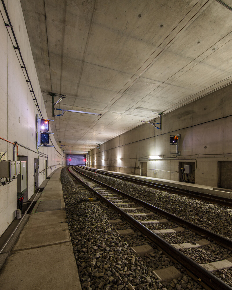 Inside a tunnel with tracks, emergency lights, doors and the far tunnel exit.